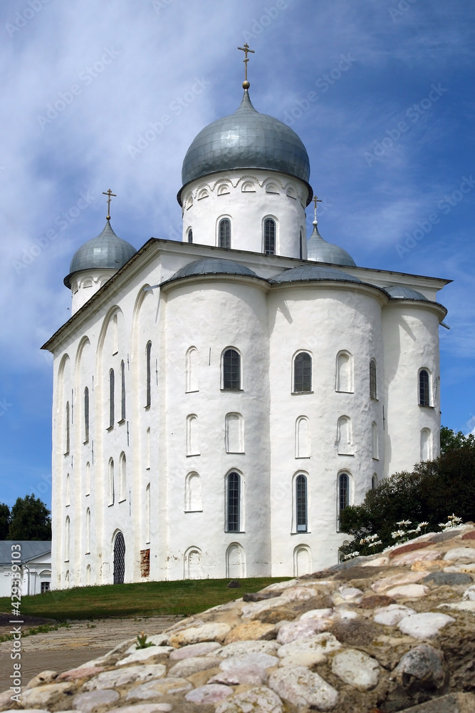 Old white church against the blue sky. There is a natural stone embankment in front of the Orthodox Church. 