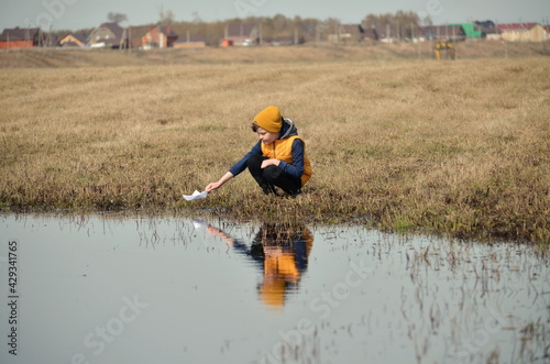 In a large puddle, a child launches a paper boat.