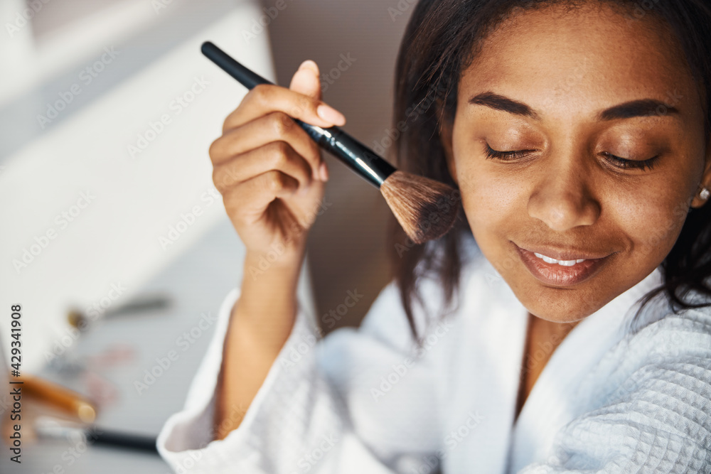 Cheerful young woman doing makeup at home