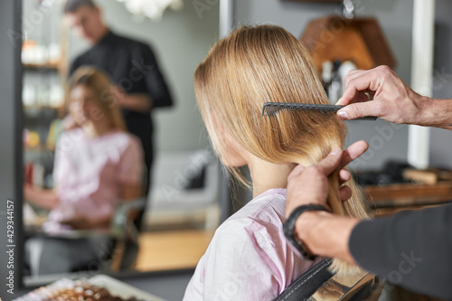 Pofessional hairdresser is combing a hair of beautiful caucasian blonde woman in modern salon