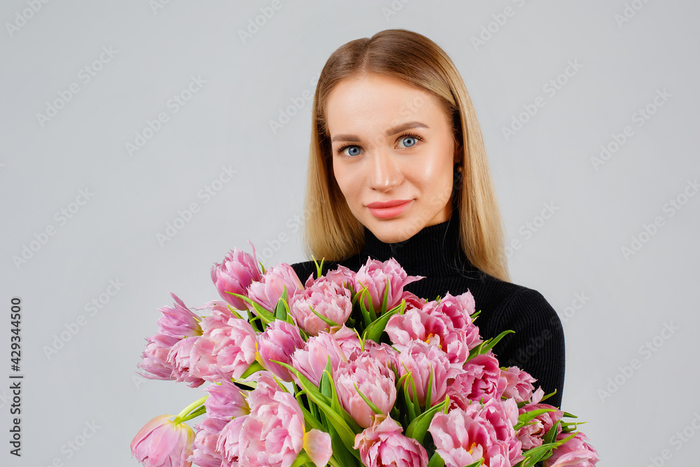 Portrait of a beautiful young woman in dark with pink tulips on a gray background, floristics