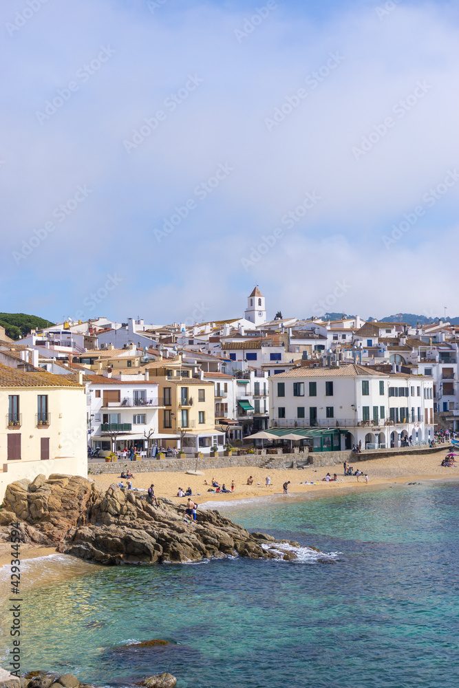 People in the sand on the beach and on the rocks in front of the Mediterranean Sea in the town of CALELLA DE PALAFRUGELL in COSTA BRAVA