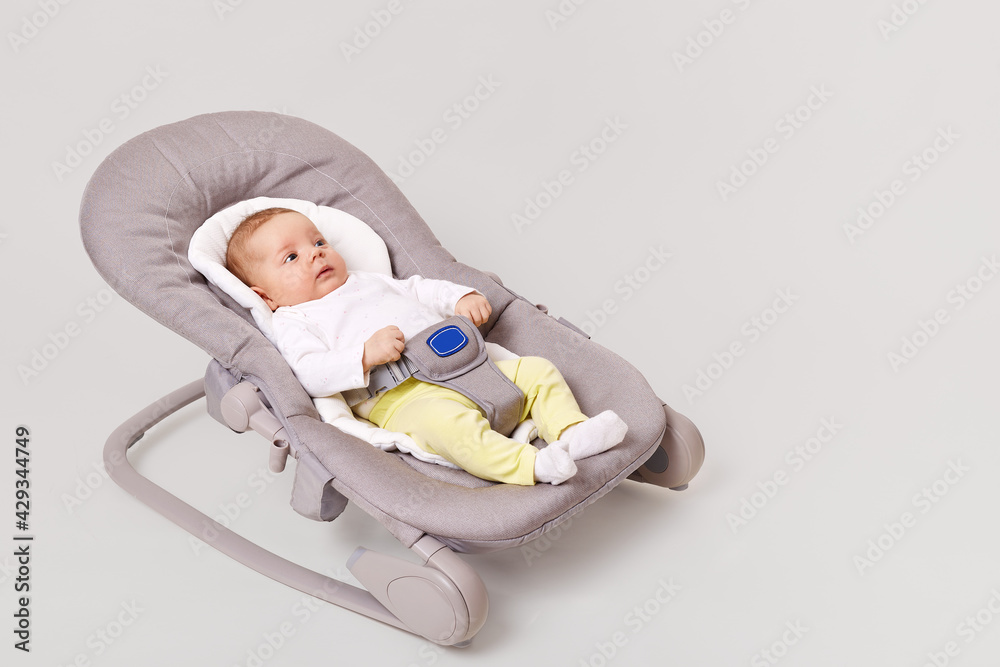 Side view of charming new born girl lying in bounce child bouncer chair little baby in tiny clothes shirt and yellow pants infant lying in rocking chair isolated over white background sementsova321