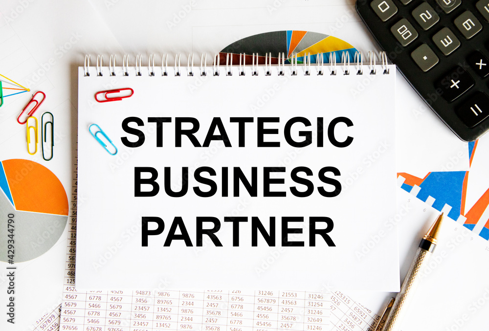 In the notebook, the text STRATEGIC BUSINESS PARTNER, the background is reports, calculator, pen, paper clips. In the notebook, the text STRATEGIC BUSINESS PARTNER, the background is reports, calculator, pen, paper clips.
