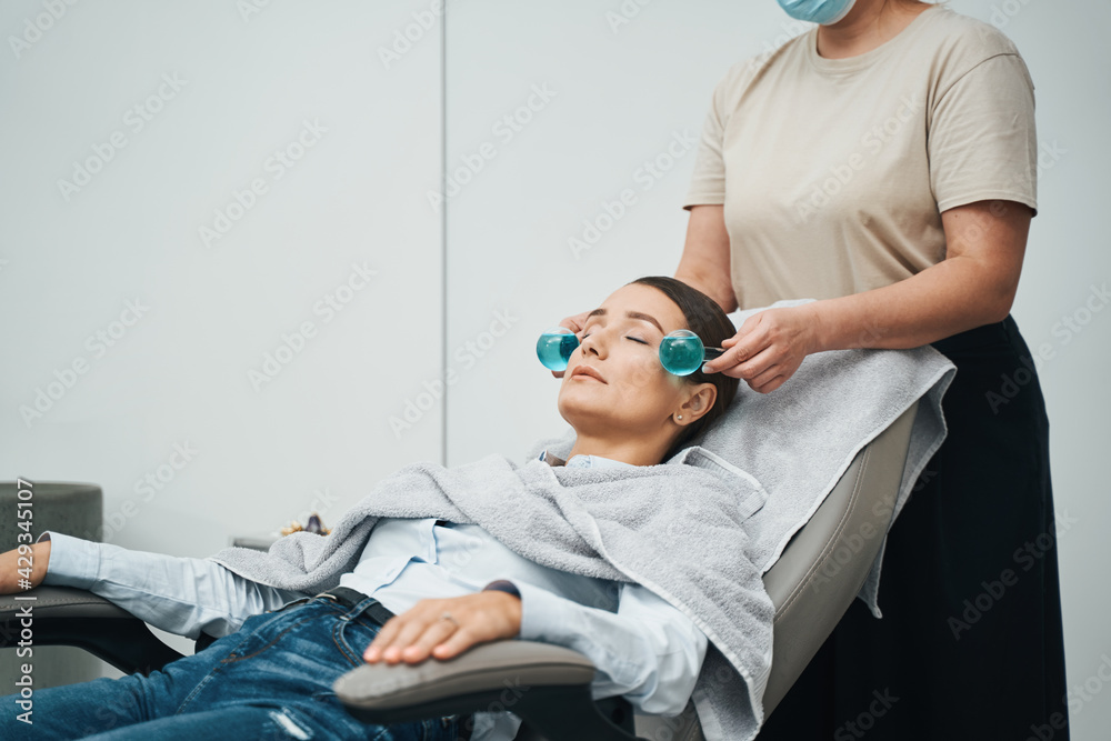 Cosmetician massaging a female face with two ice globes Cosmetician massaging a female face with two ice globes