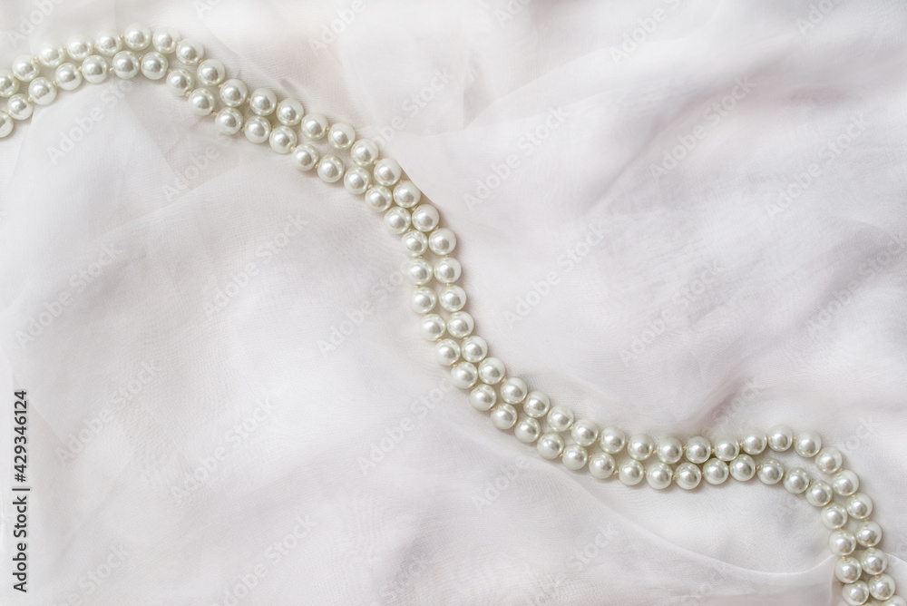 A necklace of pearls lies on a white cloth
A necklace of pearls lies on a white cloth