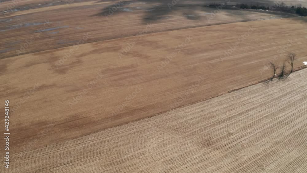Shadows of trees on brown farm fields in spring. Aerial view of cultivated land of commercial farm in plains. Wet, brown farmland ready to be plowed and prepared for early season planting. Shadows of trees on brown farm fields in spring. Aerial view of cultivated land of commercial farm in plains. Wet, brown farmland ready to be plowed and prepared for early season planting.