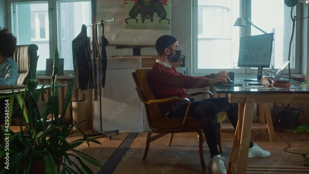 Creative Modern Office with Two Young People Wearing Face Masks Working on Computers. Business Team of Authentic Creators, Developers, Marketing Specialists Creating Content. Tracking Dolly Two Shot Creative Modern Office with Two Young People Wearing Face Masks Working on Computers. Business Team of Authentic Creators, Developers, Marketing Specialists Creating Content. Tracking Dolly Two Shot