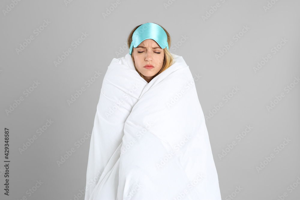 Young woman in sleeping mask wrapped with soft blanket on grey background Young woman in sleeping mask wrapped with soft blanket on grey background