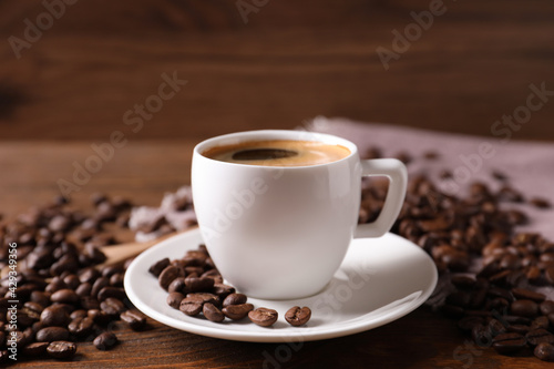 Cup of hot aromatic coffee and roasted beans on wooden table, closeup © New Africa