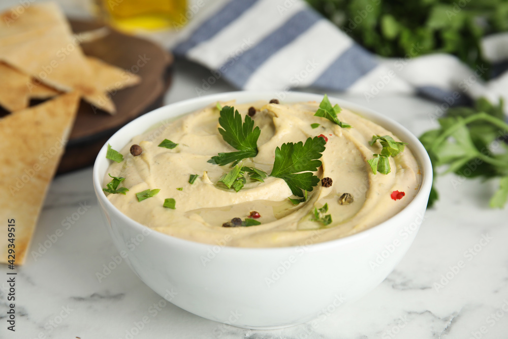 Delicious hummus with parsley and pita chips on white marble table, closeup