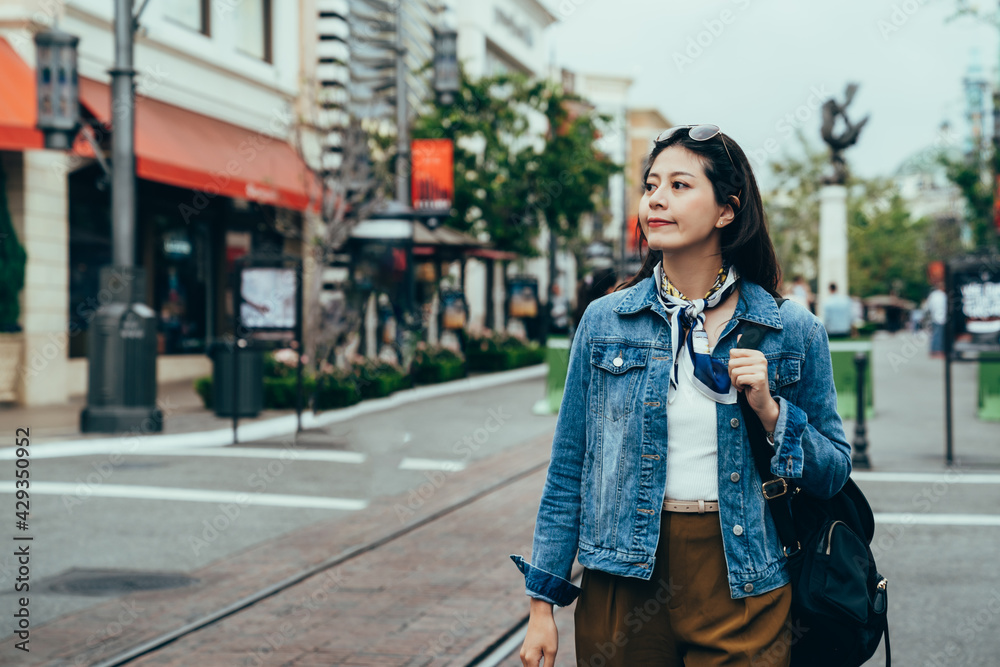 woman backpacker with sunglasses on head is appreciating the beauty of the small town. female commuter is looking at surroundings along the street on her way to school.