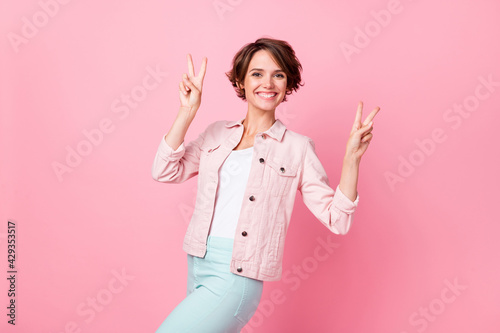 Photo of young beautiful lovely happy cheerful smiling positive girl showing v-sign isolated on pink color background © deagreez