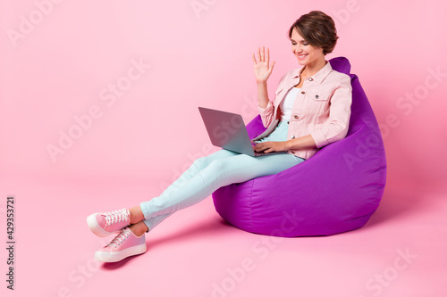 Full size photo of young beautiful lovely happy smiling girl sit armchair have video call isolated on pink color background