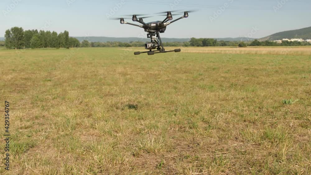 UAV drone lands in a field. Propellers rotate and then stop. Landing on a grassy area, in the background are mountains. Summer day in 4K UAV drone lands in a field. Propellers rotate and then stop. Landing on a grassy area, in the background are mountains. Summer day in 4K