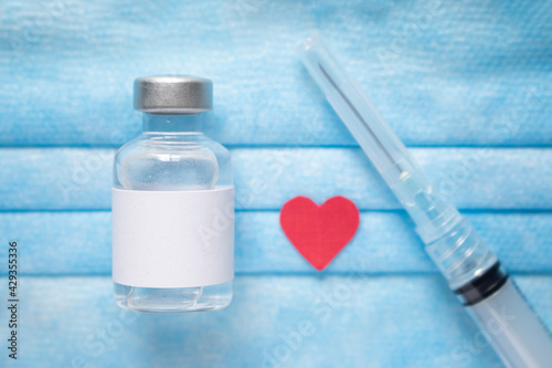 Medical vial of injectable medicine, syringe and paper red  hearton a blue medical mask