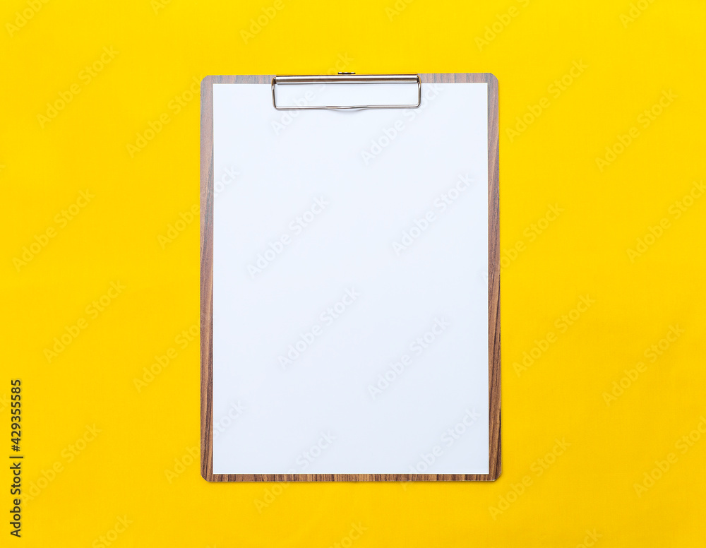 Wooden clipboard with blank paper white paper on yellow fabric background, blank paper sheet, office tool Wooden clipboard with blank paper white paper on yellow fabric background, blank paper sheet, office tool