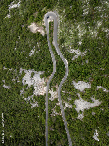 Aerial top down view of forest winding road in mountains, Montenegro. Long curving road on hills, rich vegetation, Mediterranean bush. Mountain ranges on the horizon. Summer. Travel on nature