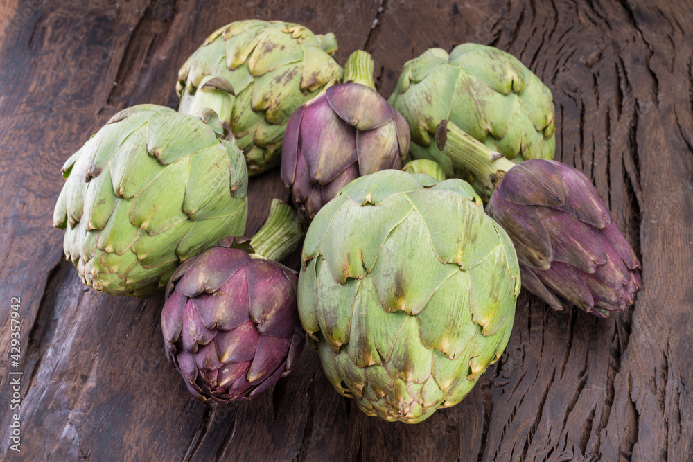 Green and purple artichoke flower edible buds on wooden background.