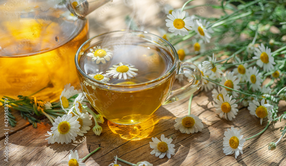 Glass of herbal chamomile tea and chamomile flowers near teapot. Close-up. Glass of herbal chamomile tea and chamomile flowers near teapot. Close-up.