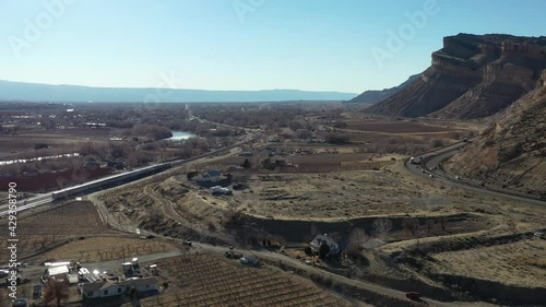 Aerial 4K view of interstate and train tracks heading west towards Grand Junction along the Palisades in Colorado. Drone shot rising up and tilting down while cars and trucks travel along interstate. photo