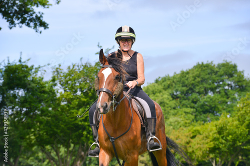 Close up shot of happy smiling woman riding her beautiful bay horse in the English countryside on a summers day.