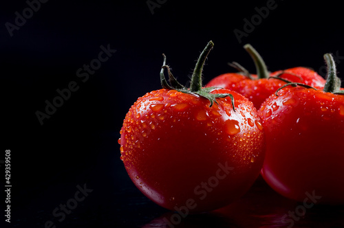 Fresh red tomatoes with drops of water on black background.