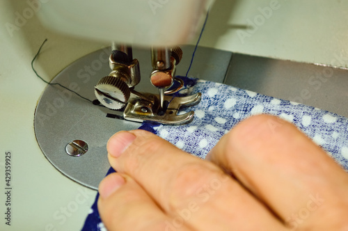 Bild auf Leinwand close-up - a woman's hand at work on a sewing machine, sews from blue material