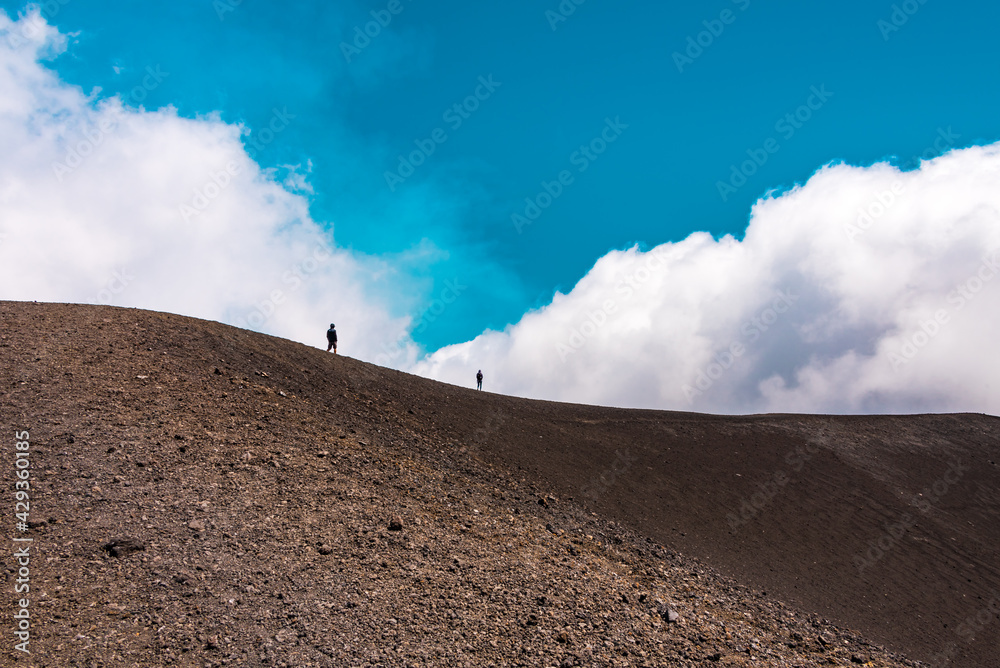 People on the edge of a volcanic crater, blue sky in the background 