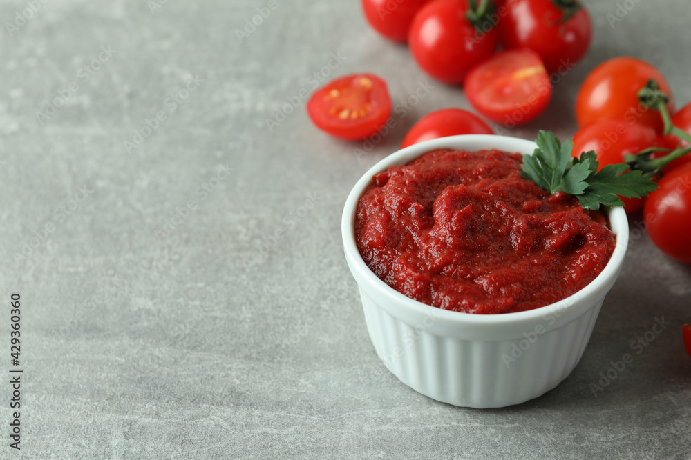 Bowl of tomato paste and tomatoes on gray textured background Bowl of tomato paste and tomatoes on gray textured background