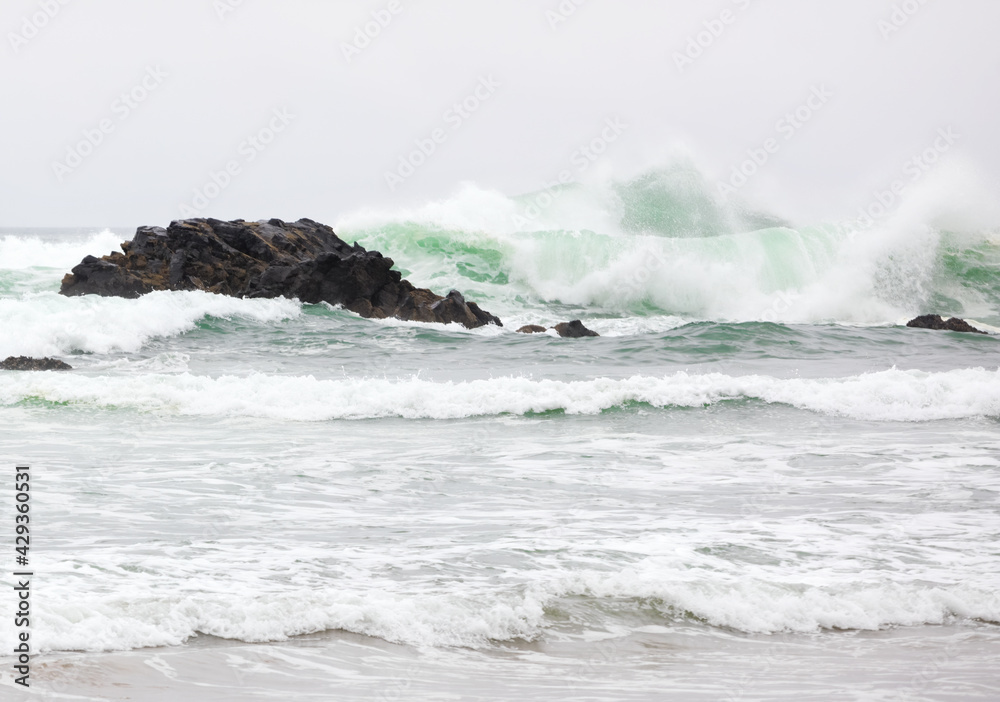 Beautiful emerald green waves of Pacific Ocean hitting rocky shore
