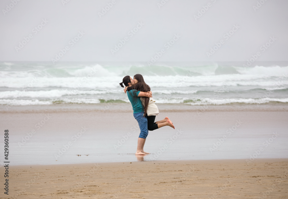 Young couple kissing on beach by ocean on foggy day Young couple kissing on beach by ocean on foggy day