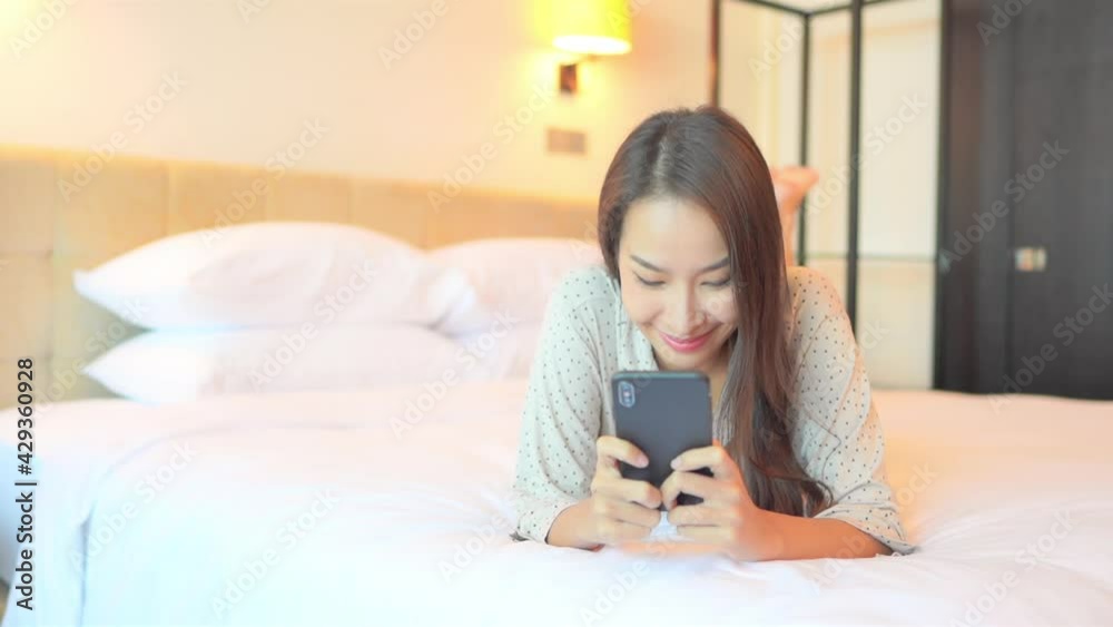 Asian woman texting on mobile phone in bed, a young happy female typing messages on smarthone, full frame Asian woman texting on mobile phone in bed, a young happy female typing messages on smarthone, full frame