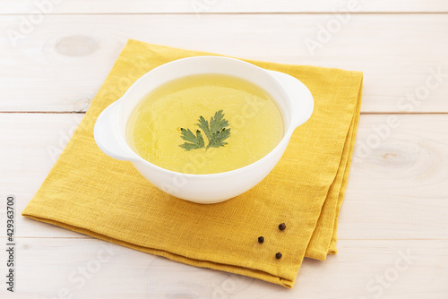 Bone broth with parsley in a bowl on a yellow napkin.