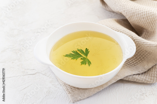 Homemade chicken bone broth with parsley in a white bowl with a towel.