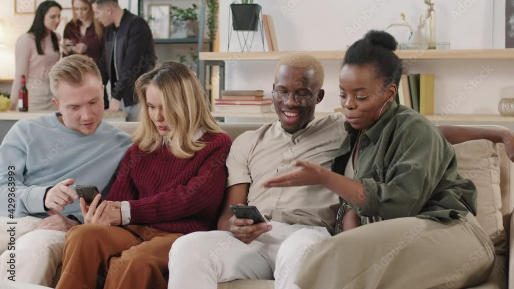 Slowmo shot of two couples sitting on couch and chatting while looking at mobile phones Slowmo shot of two couples sitting on couch and chatting while looking at mobile phones