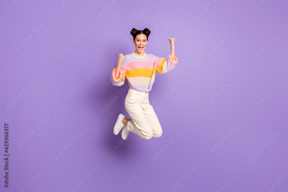 Full length photo of girlish lucky young lady dressed striped sweater jumping rising fists isolated violet color background