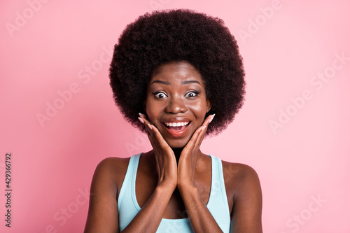 Portrait of impressed brunette curly lady hands face wear blue top isolated on pastel pink color background