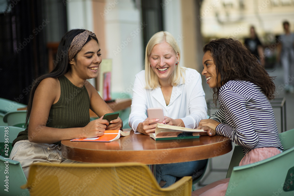 Fototapeta premium Three students reading books in café and talking. Focus is on background.