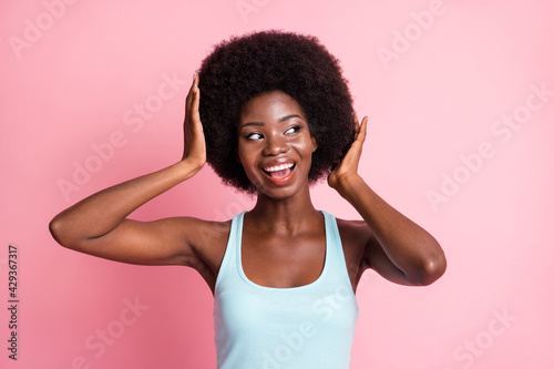 Portrait of optimistic brunette curly lady hand hair look empty space wear blue top isolated on pink color background