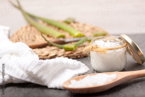 Принти на полотні Concepto de un tarro de crema de manos de aloe vera con una cuchara con la crema de manos de aloe vera y un salvamanteles desenfocado con trozos de aloe vera cortados