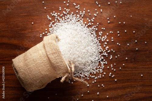 Close-up of organic white sago or sabudana small size spilled out from a laying jute bag over a wooden brown background. photo