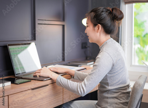 Young asian woman in casual clothes looking on laptop screen and typing financial project