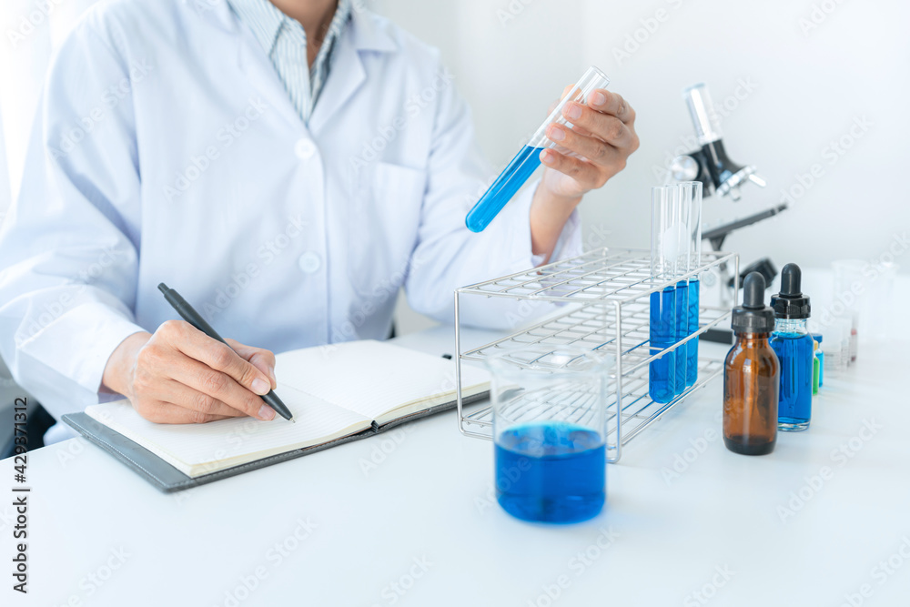 Scientist woman holding test tube in her hands and writing down result report on notebook while working