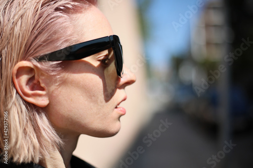 Headshot of young woman with pinkish hair, wearing sunglasses.