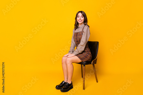 Full size profile photo of optimistic funny brunette lady sit wear shirt dress sneakers isolated on vivid yellow background