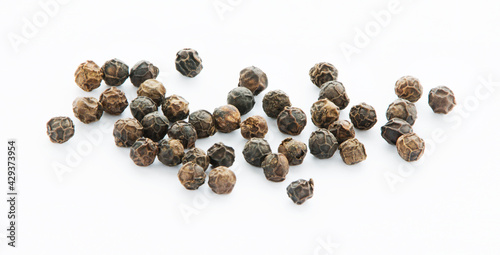 Dry seeds of black pepper on a white surface in close up.  Spice. Ingredients. Condiments.  
