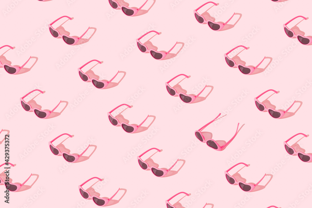 Minimal pattern made of pink sunglasses with sunlight shadow on pastel pink background. Creative summer concept.