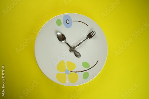 silver wares spoon and fork with cute white ceramic plate on bright yellow background clock like pattern