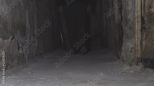 Man walking down the dark corridor of an old abandoned basement. Front view. Low key